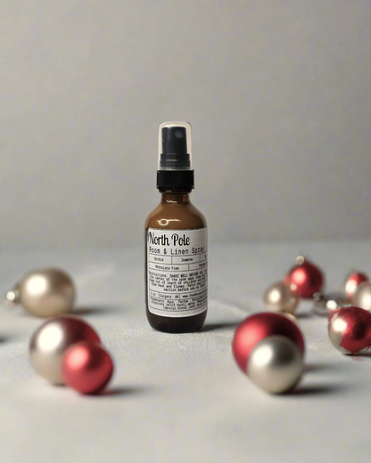 North Pole Room & Linen Spray 2 oz bottle, capturing winter holiday scents of eggnog, peppermint, cinnamon, and pinecones. Phthalate-free, paraben-free, and no alcohol content, safe for room and linen use. Front view of the bottle next to winter décor.