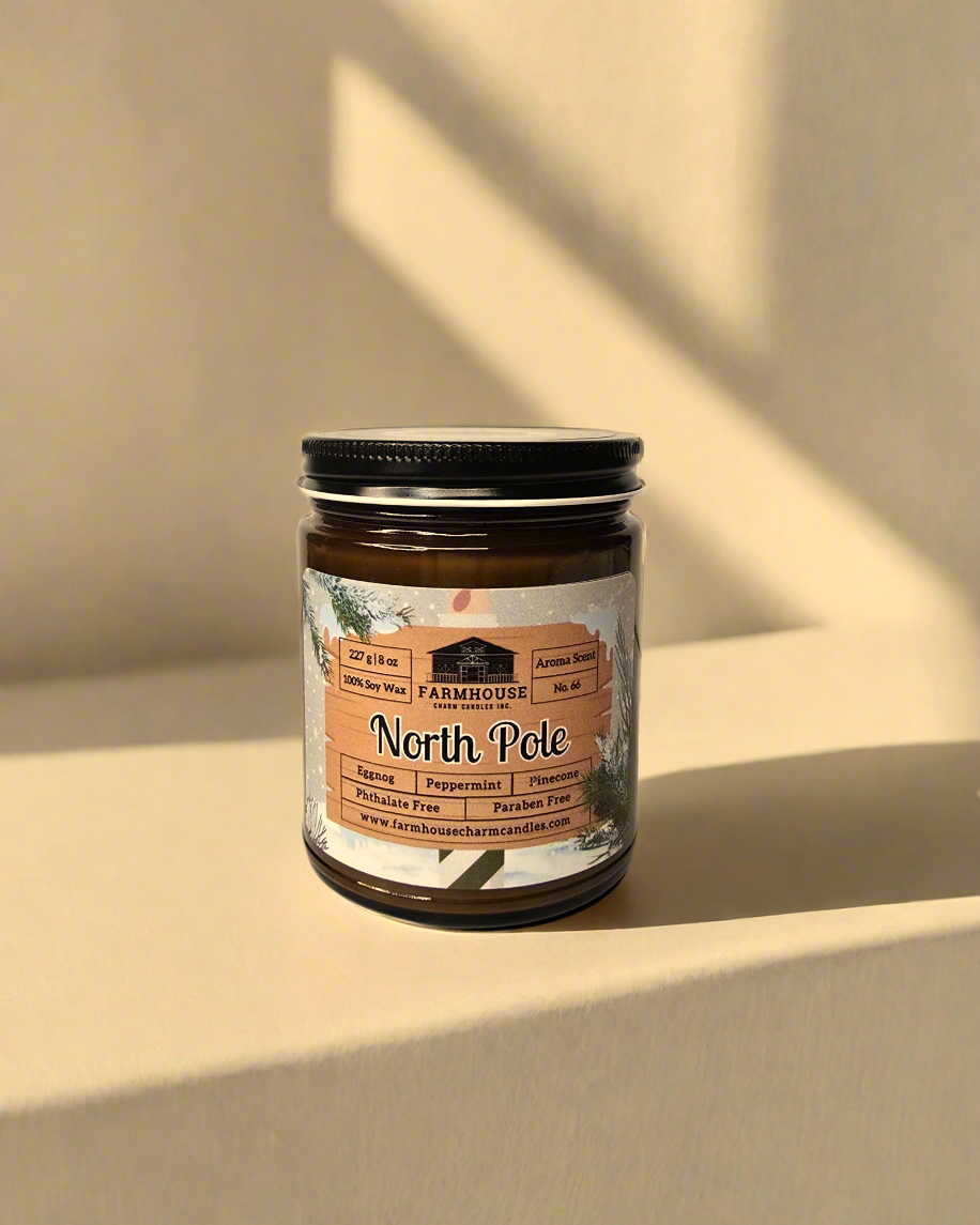 North Pole Soy Candle by Farmhouse Charm Candles, an 8 oz natural soy wax candle featuring a blend of buttery eggnog, peppermint, cinnamon, and pinecone scents, with a crackling wooden wick for up to 50 hours of burn time, presented in an eco-friendly amber jar.