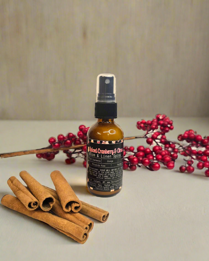 Spiced Cranberry Room and Linen Spray bottle displayed with festive background, featuring seasonal scents of tart cranberry, mulberry, tangy orange, spicy clove, and warm cinnamon. Perfect for adding a cozy and refreshing holiday aroma to any room or fabric.